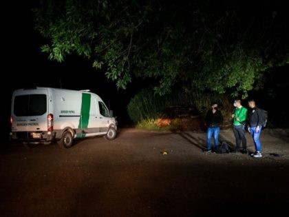 Three migrant men wait for transportation after being apprehended near the border between