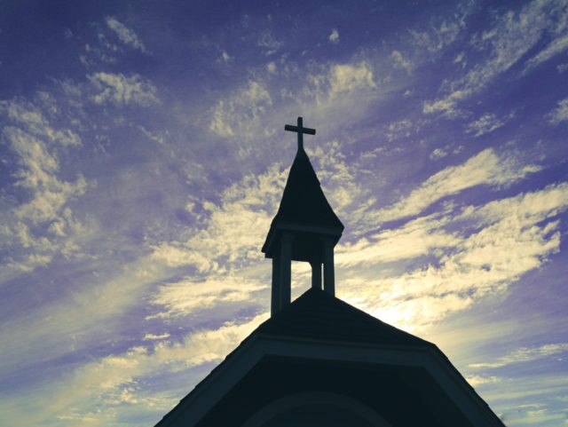 heavenly religious church chapel steeple in silhouette against a azure blue purple cloudscape sky