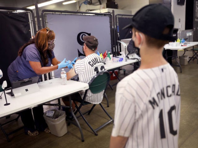 CHICAGO, ILLINOIS - JUNE 08: Gavin Feltz, 11, watches as his father Robert Feltz gets a COVID-19 vaccine from Delearna Jackson at Guaranteed Rate Field before the start of the Chicago White Sox game against the Toronto Blue Jays on June 08, 2021 in Chicago, Illinois. Fans who received the …