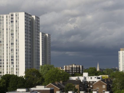A variety of low, medium and high rise social housing types in north London, England.High rise apartments tower over local authority housing and flats amidst a splash of green trees. The tower blocks are lit by the evening sun against a backdrop of ominous black storm clouds