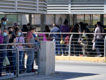Travelers, left, waiting in line to cross a customs area into the United States at the McAllen-Hidalgo International Bridge look on as a group of migrants, right, are deported to Reynosa, Mexico, Thursday, March 18, 2021, in Hidalgo, Texas. A surge of migrants on the Southwest border has the Biden …