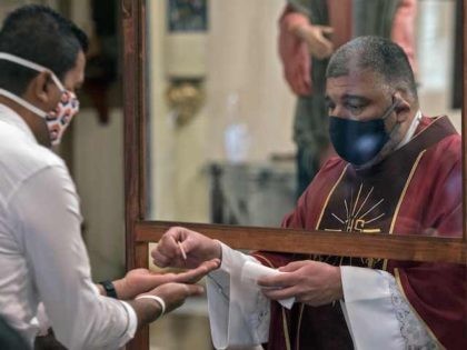 A priest wearing a face mask gives a communion host to a man with a glass in between them during a mass at the Basilica de los Angeles in Cartago, Costa Rica, June 28, 2020, amid the new coronavirus pandemic. - The third phase of measures against the spread of …