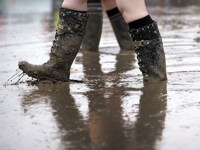 A festival goer in wellies walks through a muddy puddle as she makes her way through the s