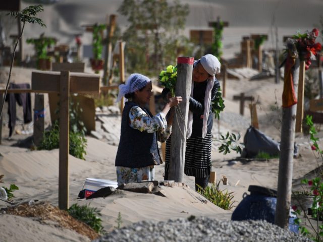 TOPSHOT - This photo taken on May 31, 2019 shows two women decorating a grave in a Uighur graveyard on the outskirts of Hotan in China's northwest Xinjiang region. - China has enforced a massive security crackdown in Xinjiang, where more than one million ethnic Uighurs and other mostly Muslim …