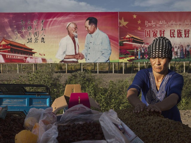 An ethnic Uyghur woman arranges raisins for sale at her stall with a billboard showing the