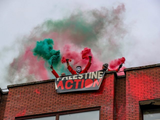 Palestine Action activists light flares as they hold a banner "Palestine Action" after they scaled the roof of "Cairo House" in Oldham on Monday, June 21, 2021. This is the ongoing protest forms of the human rights activists group in Britain targeting an Israeli owned weapons manufacturer Elbit Systems. Activists …