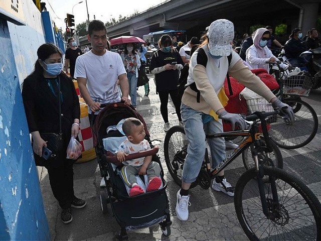 A couple pushes their child in a stroller between bicycles at a busy intersection in Beijing on June 2, 2021, days after China announced it would allow couples to have three children. (Photo by GREG BAKER / AFP) (Photo by GREG BAKER/AFP via Getty Images)