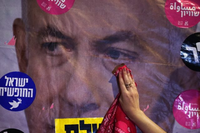 An Israeli protester mimics wiping a tear off a poster depicting Prime Minister Benjamin N