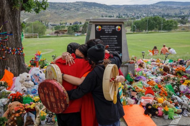 People from Mosakahiken Cree Nation hug in front of a makeshift memorial at the former Kam