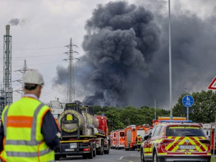 Emergency vehicles of the fire brigade, rescue services and police stand not far from an access road to the Chempark over which a dark cloud of smoke is rising in Leverkusen, Germany, Tuesday, July 27, 2021.. After an explosion, fire brigade, rescue services and police are currently in large-scale operation, …