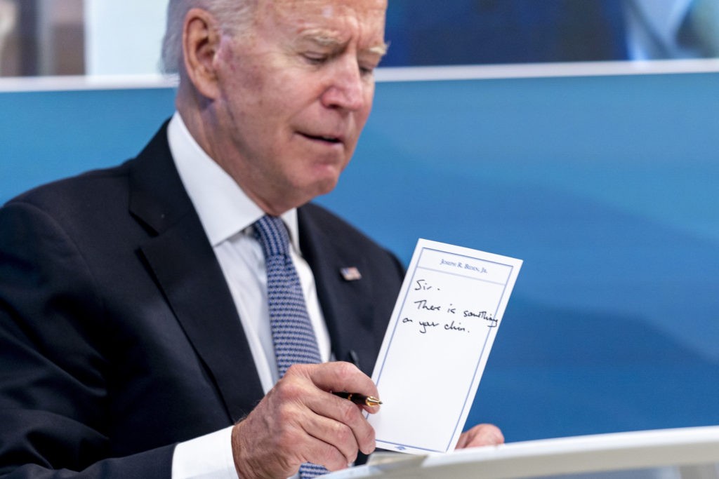President Joe Biden holds a card handed to him by an aide that reads 