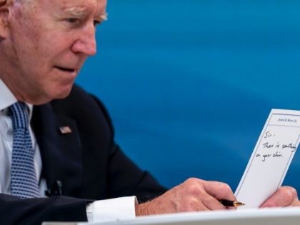 President Joe Biden holds a card handed to him by an aide that reads "Sir, there is someth