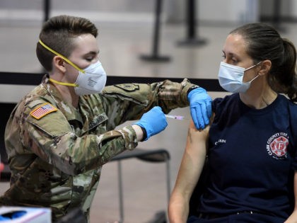 LAS VEGAS, NEVADA - JANUARY 14: Spc. Katherine Deskins (L) of the Nevada Army National Guard administers a Moderna COVID-19 vaccination to Clark County Fire Department Capt. Jasmine Ghazinour on the first day of Clark County's pilot vaccination program at Cashman Center on January 14, 2021 in Las Vegas, Nevada. …