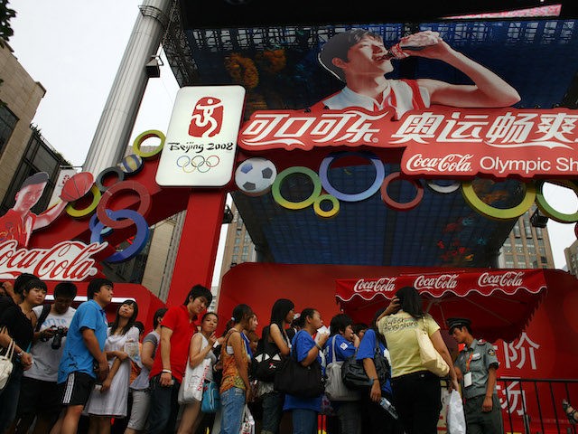 BEIJING, CHINA-AUGUST 19: People wait in line at the Olympic Shuang Zone as Chinese hurdler Liu Xiang, sponsored by Coca Cola is seen drinking the soda on a billboard August 19, 2008 in Beijing. According to Xinhua agency, Liu Xiang has said he will run even faster after he fully …