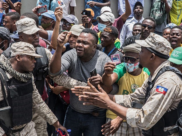 Police try to hold people back as supporters cheer and surround an ambulance carrying former Haitian President Jean-Bertrand Aristide after he arrived at the airport in Port-au-Prince on July 16, 2021, after spending nearly a month in Cuba for medical treatment. (Photo by Valerie Baeriswyl / AFP) (Photo by VALERIE …