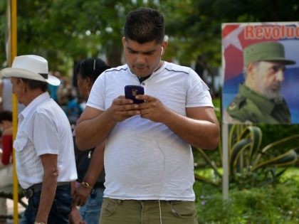 TOPSHOT - A man connects to internet from his mobile phone in Havana, on March 17, 2019, with a sign depicting Cuban late leader Fidel Castro in the background. - A new civil society emerges in Cuba with mobile phones having internet, defying six decades of unanimity. (Photo by YAMIL …