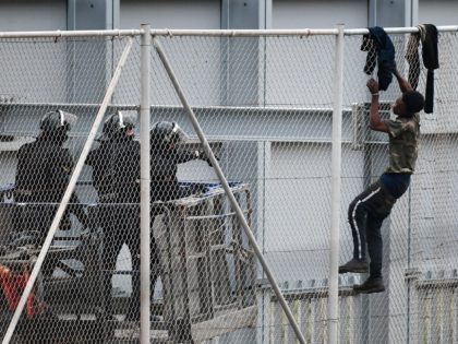 TOPSHOT - A youth tries to climb over the border fence in the Spanish exclave of Ceuta bor