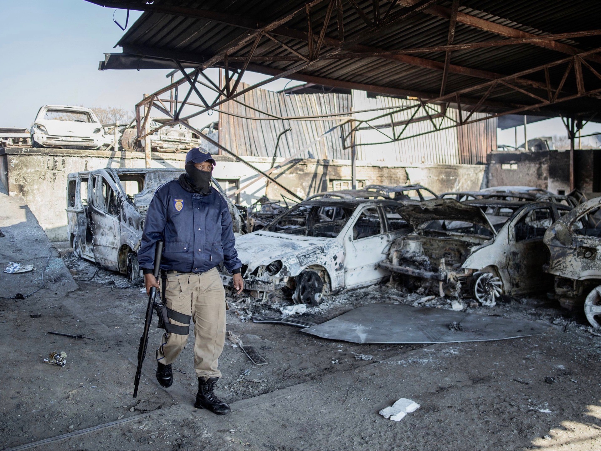 A Johannesburg Metro Police Department (JMPD) officer walks past the wreckage of burnt cars at a car showroom in Jeppestown district, Johannesburg, on July 11, 2021. - Several shops are damaged and cars burnt in Jeppestown, Johannesburg, following a night of violence. Police are on the scene trying to control further protests. It is unclear if this is linked to sporadic protests following the incarceration of former president Jacob Zuma. (Photo by LUCA SOLA / AFP) (Photo by LUCA SOLA/AFP via Getty Images)