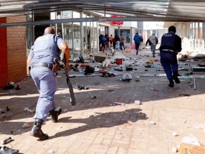 People flee from police as they carry goods while looting and vandalising the Lotsoho Mall in Katlehong township, East of Johannesburg, on July 12, 2021. - Several shops are damaged and cars burnt in Johannesburg, following a night of violence. Police are on the scene trying to control further protests. …
