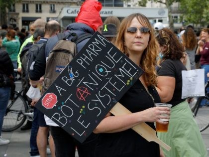TOPSHOT - A woman holds a placard hostile to Pharmaceutical firms as she takes part in a gathering at Republic square in Paris on July 14, 2021 to protest against a governmental decision to impose Covid-19 tests for unvaccinated people who want to eat in restaurants or take long-distance trips, …