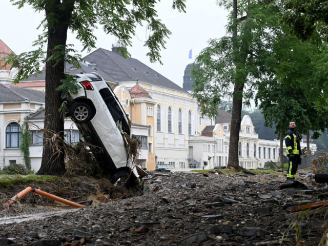 A fireman stands next to a destroyed car pressed against a tree by the torrents after the floods caused major damage in Bad Neuenahr-Ahrweiler, western Germany, on July 16, 2021. - The death toll from devastating floods in Europe soared to at least 118 on July 16, with at least …