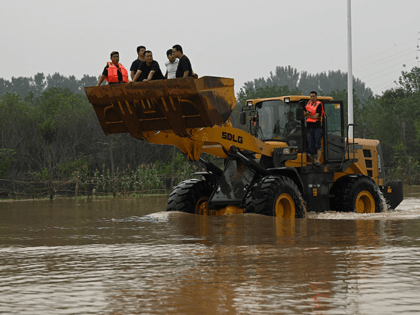 People ride on the front of a loader to cross a flooded street following a heavy rain that flooded and claimed the lives of at least 33 people earlier in the week, in the city of Zhengzhou, in China's Henan province on July 23, 2021. (Photo by Noel Celis / …