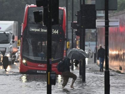A pedestrian crosses through deep water on a flooded road in The Nine Elms district of London on July 25, 2021 during heavy rain. - Buses and cars were left stranded when roads across London flooded on Sunday, as repeated thunderstorms battered the British capital. (Photo by JUSTIN TALLIS / …