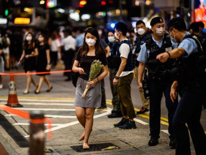 This picture taken in Hong Kong on July 2, 2021 shows police directing a woman holding flowers out from a cordoned zone, after checking her identity in the shopping district of Causeway Bay, near the site where a man stabbed a police officer in the back the night before, before …