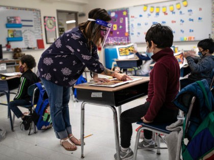 STAMFORD, CONNECTICUT - SEPTEMBER 16: Teacher Elizabeth DeSantis, wearing a mask and face shield, helps a first grader during reading class at Stark Elementary School on September 16, 2020 in Stamford, Connecticut. Most students at Stamford Public Schools are taking part in a hybrid education model, where they attend in-school …