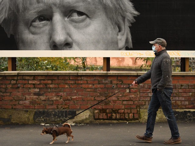 A man wearing a protective face mask walks his dog past a billboard showing Britain's Prime Minister Boris Johnson in Manchester, north-west England on November 6, 2020, as the second lockdown comes into force in England. - A united effort to tackle spiking coronavirus infection rates has been called for …