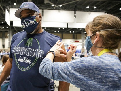 Cleveland Hughes wears Seahawks gear as he gets the Pfizer Covid-19 vaccine from Andrea Barnett during opening day of the Community Vaccination Site, a collaboration between the City of Seattle, First & Goal Inc., and Swedish Health Services at the Lumen Field Event Center in Seattle, Washington on March 13, …