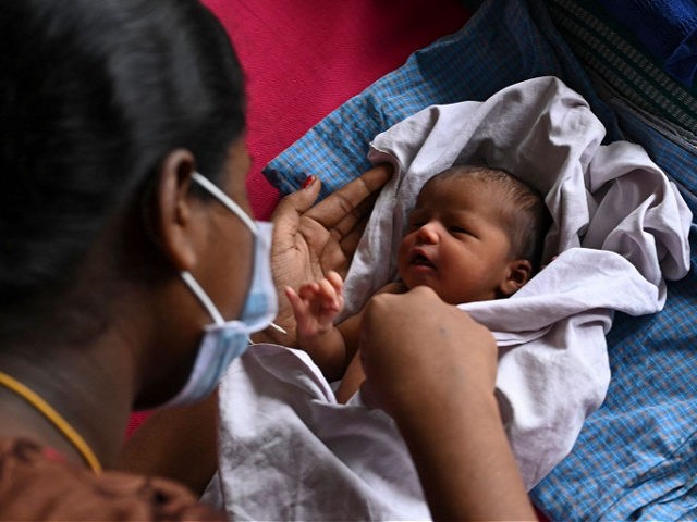 A mother, with her newborn baby, waits with other new mothers to get inoculated with a dos