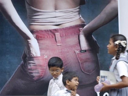 BOMBAY, INDIA: Indian school children walk past a poster advertising jeans in the streets of Bombay, 05 October 2004. Fashions, particularly for the young, are changing in the commercial capital, influenced by overseas trends and billboard advertising, yet the vast majority of women still wear the traditional saree or Salwar …