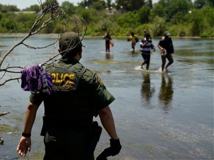 A Border Patrol agent watches as a group of migrants walk across the Rio Grande on their way to turn themselves in upon crossing the U.S.-Mexico border, Tuesday, June 15, 2021, in Del Rio, Texas. U.S. government data shows that 42% of all families encountered along the border in May …