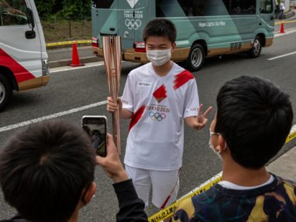 HOKUTO, JAPAN - JUNE 26: A torch bearer has his photo taken during the Tokyo Olympic Games Torch Relay on June 26, 2021 in Hokuto, Japan. As the Olympic torch relay makes its way around Japan, much of the original route has been altered or cancelled completely as prefectural authorities …