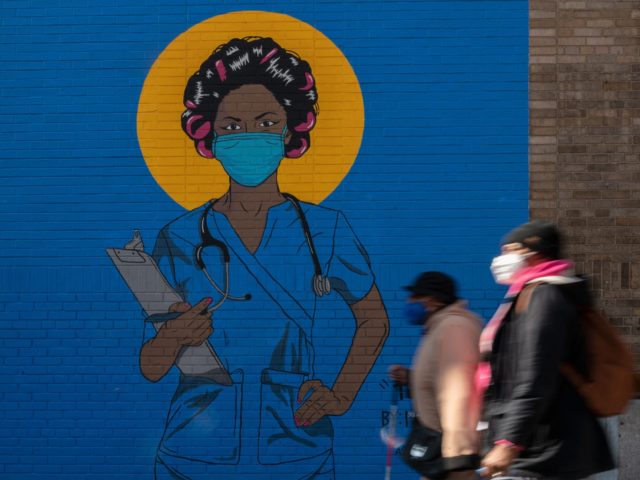 People walk past a mural by artist M. Tony Peralta picturing a healthcare worker at New York Presbyterian Hospital on March 22, 2021 in New York City. - RESTRICTED TO EDITORIAL USE - MANDATORY MENTION OF THE ARTIST UPON PUBLICATION - TO ILLUSTRATE THE EVENT AS SPECIFIED IN THE CAPTION …