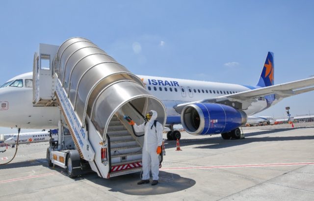 An Israeli worker in full hazmat suit sprays disinfectant on the stairs of an Israir airpl