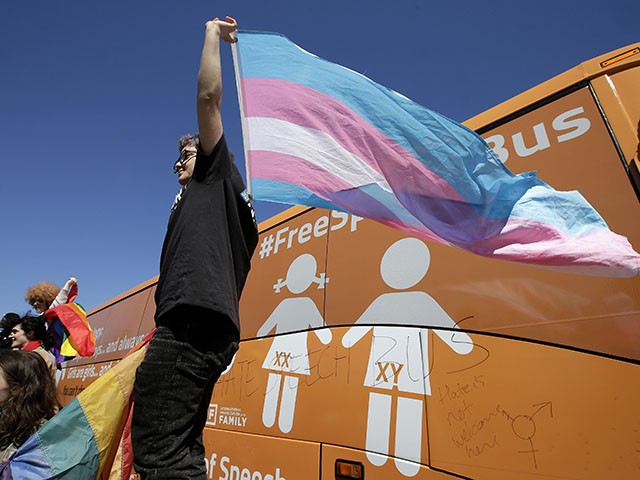 Leon Weiler, of Cambridge, Mass., top, holds a flag while standing with other protesters in support of transgender rights beside the "Free Speech Bus," painted with the words "boys are boys" and "girls are girls," in the Harvard Square neighborhood of Cambridge, Thursday, March 30, 2017. A spokesman for the group behind the bus said organizers are pushing back against greater acceptance of transgender people. (AP Photo/Steven Senne)
