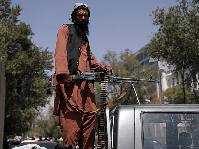 A Taliban fighter sits on the back of vehicle with a machine gun in front of the main gate