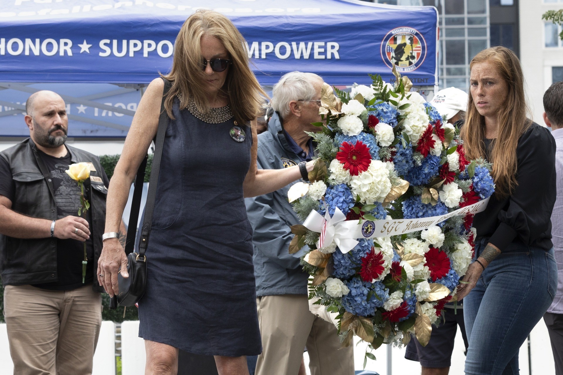 Mary Ellen Callahan, left, and Kelsey Powers, right, carry a wreath in memory of Marine Sgt. Johanny Rosario Pichardo, from Lawrence, Mass., during a ceremony at the Massachusetts Fallen Heroes Memorial, Saturday, Aug. 28, 2021, in Boston. The ceremony was held to honor the U.S. service members killed in a suicide bombing at the airport in Kabul, Afghanistan, including Rosario. (AP Photo/Michael Dwyer)