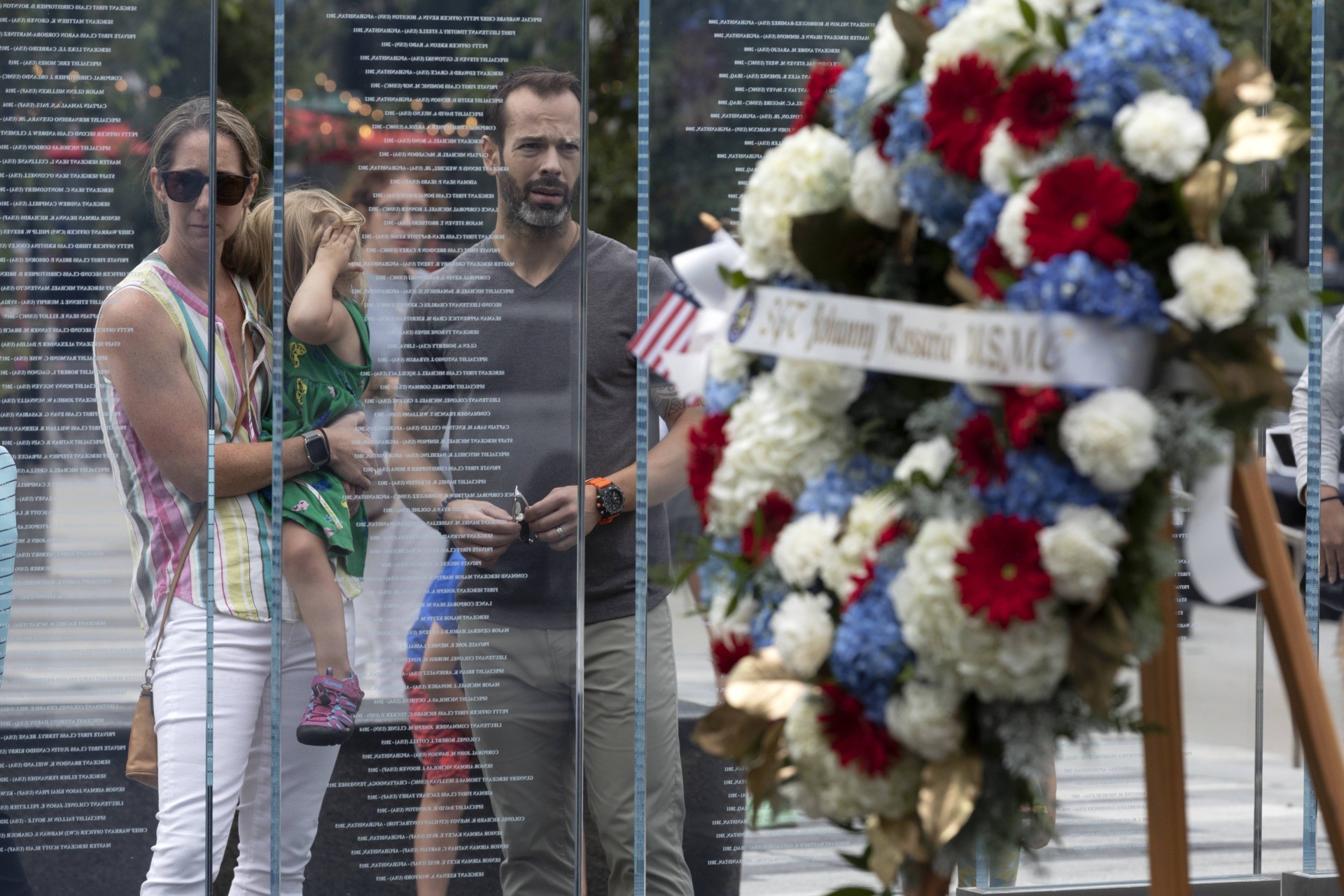 Retired Army Capt. Stephen Hunnewell stands with his wife Jessica and daughter Elizabeth behind a wreath in memory of Marine Sgt. Johanny Rosario Pichardo from Lawrence, Mass., following a ceremony at the Massachusetts Fallen Heroes Memorial, Saturday, Aug. 28, 2021, in Boston.The ceremony was held to honor the U.S. service members killed in a suicide bombing at the airport in Kabul, Afghanistan, including Sgt. Rosario Pichardo. (AP Photo/Michael Dwyer)