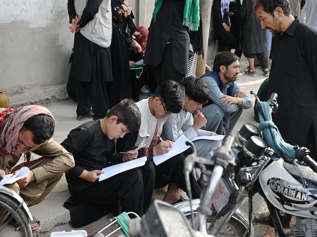 Afghan people fill up their details on a sheet of paper to register their name in order to leave the country in front of the British and Canadian embassy in Kabul on August 19, 2021, after the Taliban's military takeover of Afghanistan. (Wakil Kohsar/AFP via Getty Images)