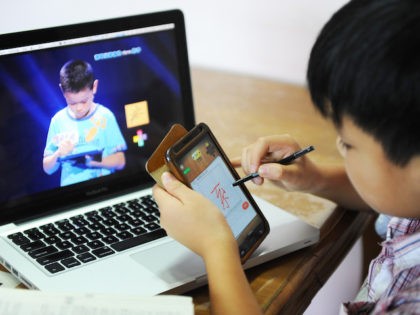 A boy writes a Chinese character on his cellphone as he watches a TV programme called "hanzi yingxiong", Chinese characters hero, at his home in Beijing on August 23, 2013. AFP PHOTO (Photo credit should read STR/AFP via Getty Images)