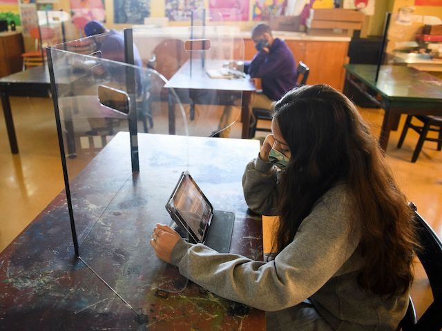 Students work behind protective barriers during an art class as they return to in-person l