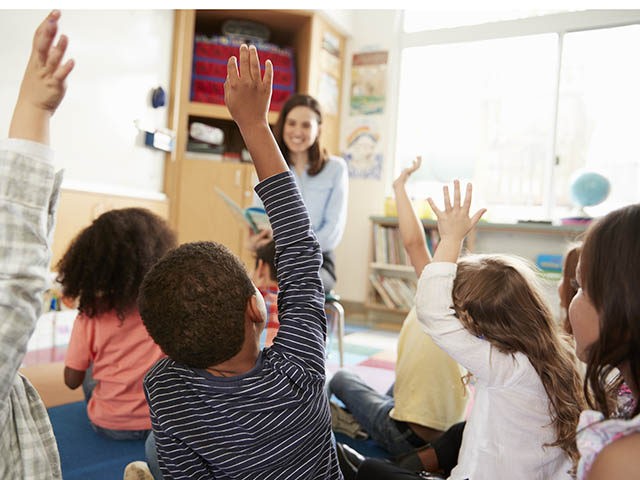 Elementary school kids raising hands to teacher, back view