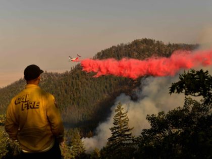 TOPSHOT - A Cal Fire firefighter from the Lassen-Modoc Unit watches as an air tanker makes a fire retardant drop on the Dixie Fire as trees burn on a hillside on August 18, 2021 near Janesville, California. - The wildfire in Northern California continues to grow, burning over 626,000 acres …