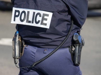 The back of the police officer with the inscription "POLICE" with a gun and a walkie-talkie. French policeman in outfit, view from the back on the street of Paris. France,