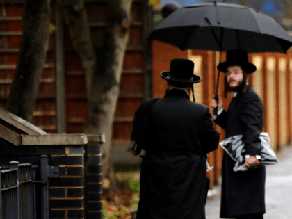 Members of the Orthodox Jewish community shelter from the rain beneath an umbrella as they