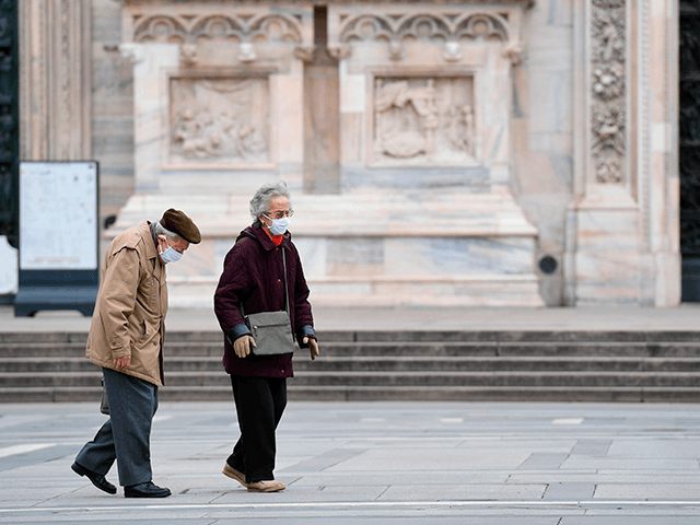 An elderly couple wearing protective masks walk across a deserted Duomo square in Milan on March 31, 2020, during the country's lockdown aimed at curbing the spread of the COVID-19 infection, caused by the novel coronavirus. (Photo by MIGUEL MEDINA / AFP) (Photo by MIGUEL MEDINA/AFP via Getty Images)