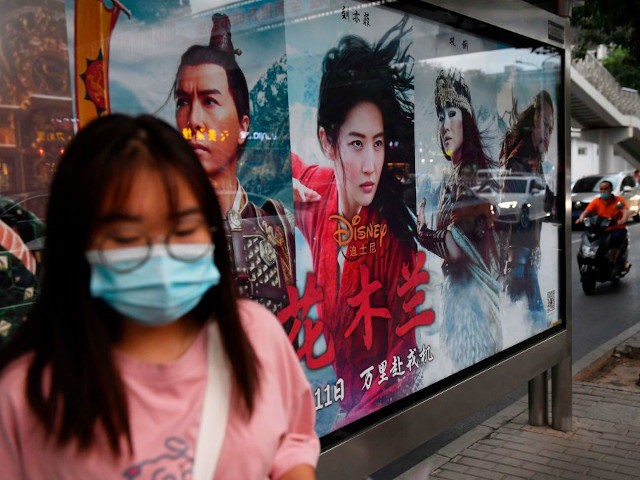A woman waits beside a poster for the Disney movie "Mulan" at a bus stop on the day the movie opened in Beijing on September 11, 2020. - Pilloried internationally and given a lukewarm debut by Chinese cinemagoers, Disney on September 11 discovered its $200 million live-action epic "Mulan" has …